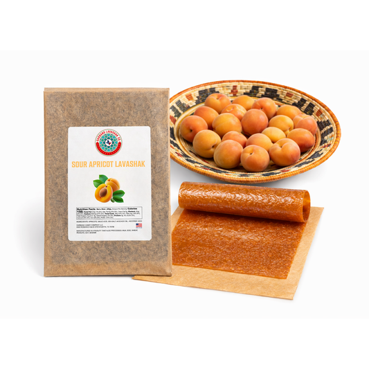 Darband Sour Apricot Lavashak — handmade Persian fruit leather in eco-friendly kraft paper packaging, shown with fresh Pacific Northwest apricots in a woven basket and a rolled sheet of golden apricot lavashak